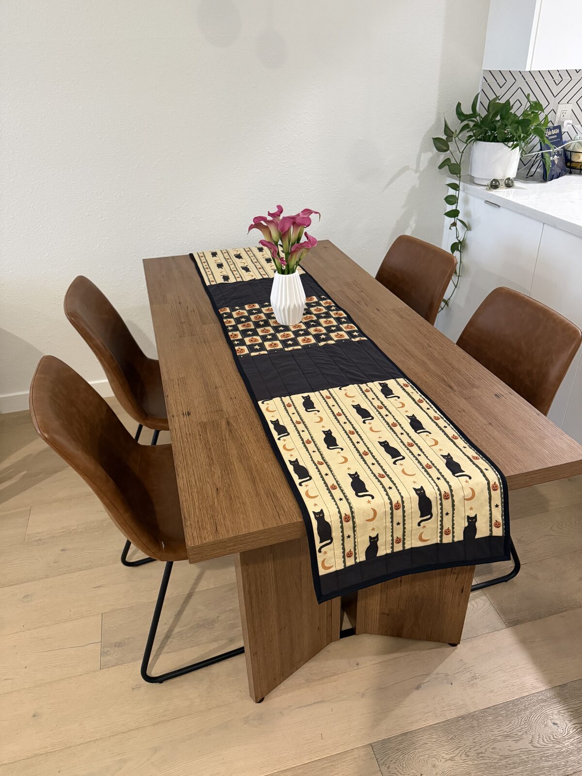 A quilted Halloween table runner in black, cream cat print, and orange pumpkin print blocks on Emily's dining table